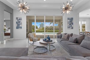 Modern open concept living room with gray sectional sofa, round glass tables, and glass doors to a backyard pool.