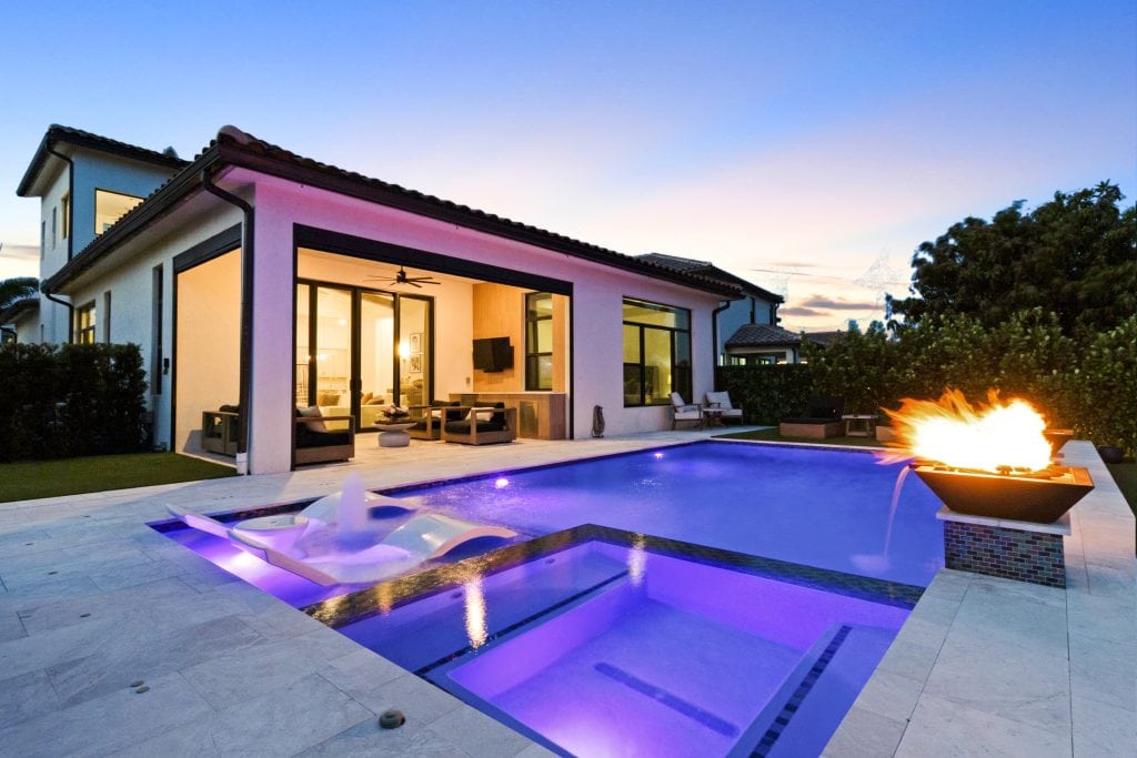 Luxury backyard with illuminated swimming pool, fire feature, and outdoor seating at dusk.