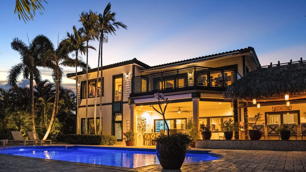 Luxury tropical villa with pool, palm trees, and outdoor living space at sunset.