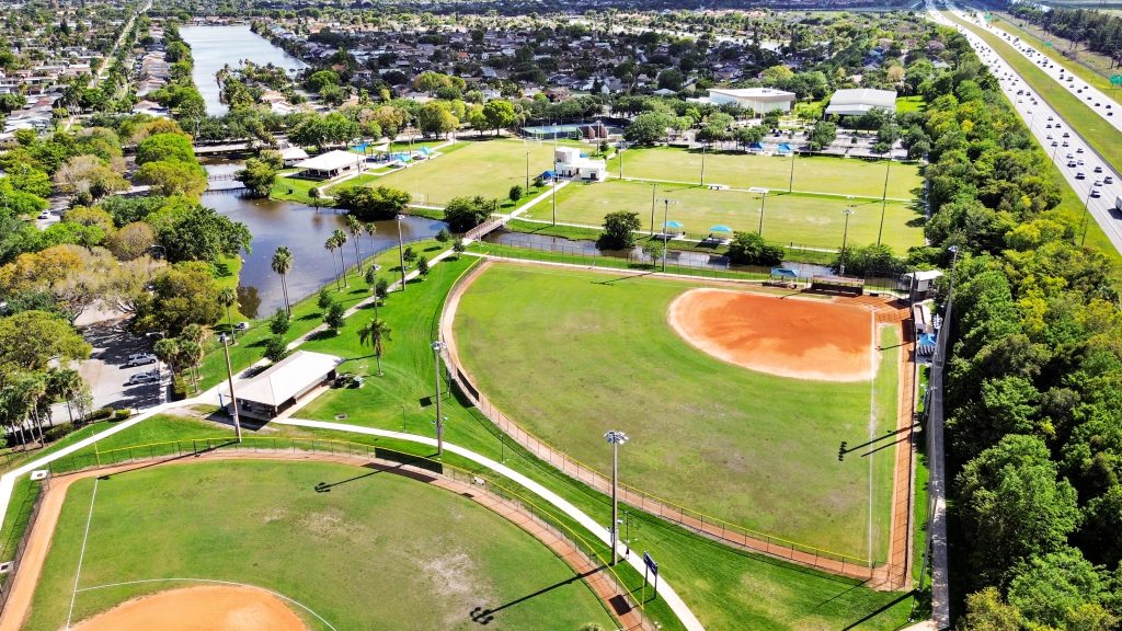 Aerial view of a city park featuring baseball diamonds, walking trails, and surrounding trees.
