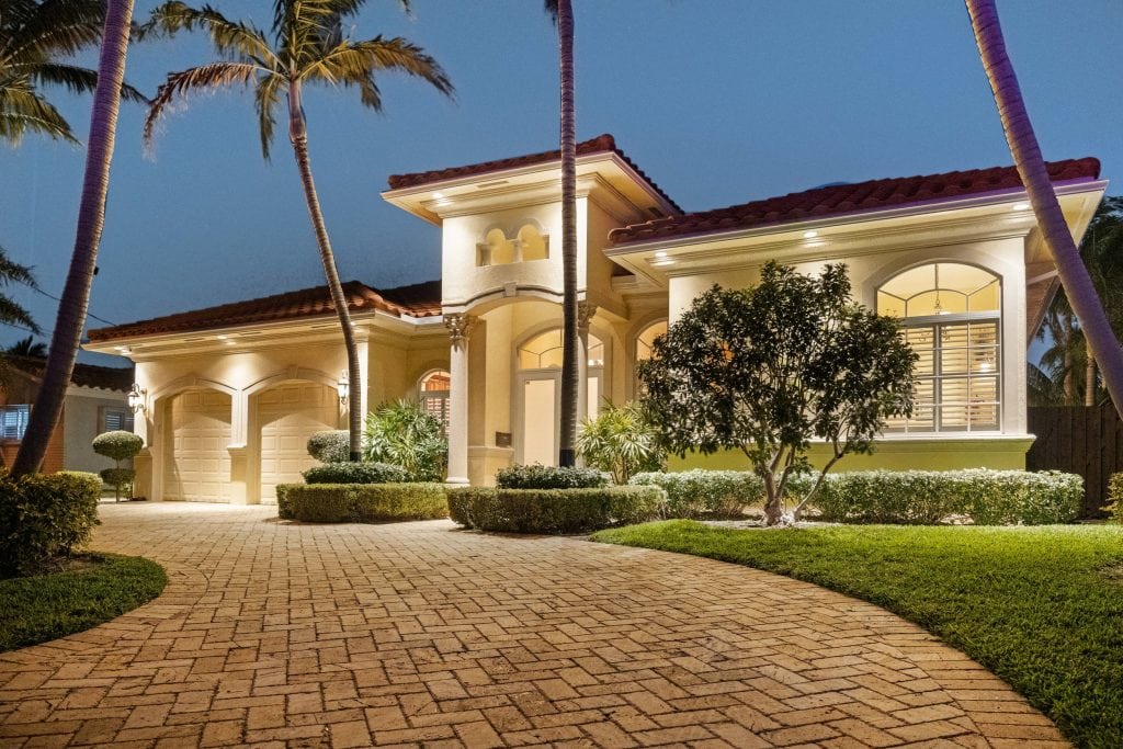 Luxury Florida home with palm trees, illuminated exterior, and well-maintained landscaping at dusk.
