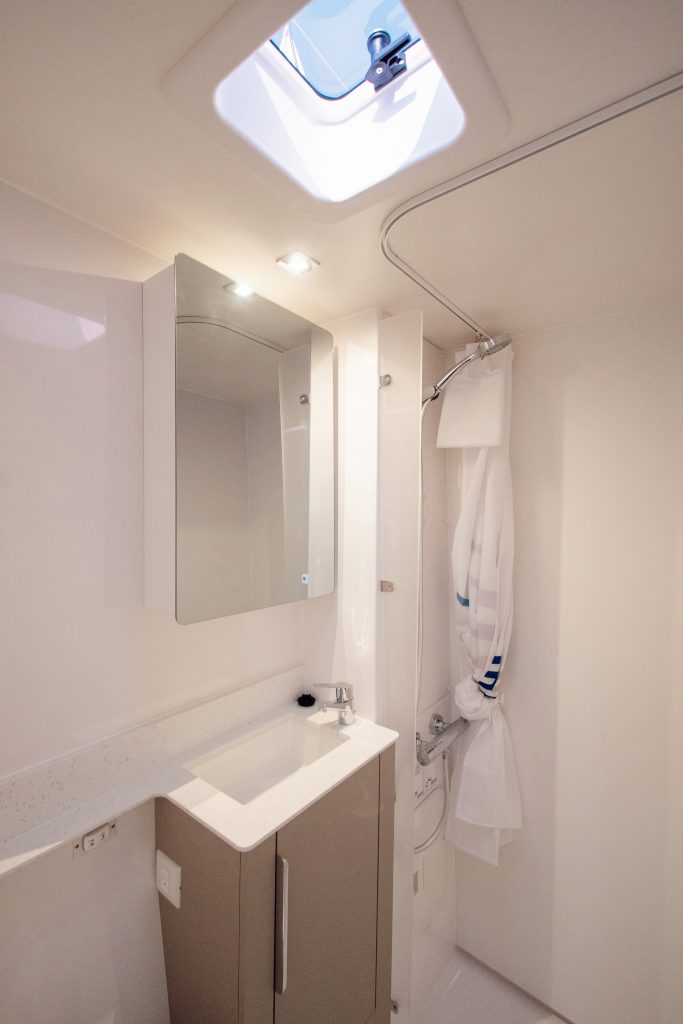 Compact yacht bathroom with skylight, mirror, and shower curtain.