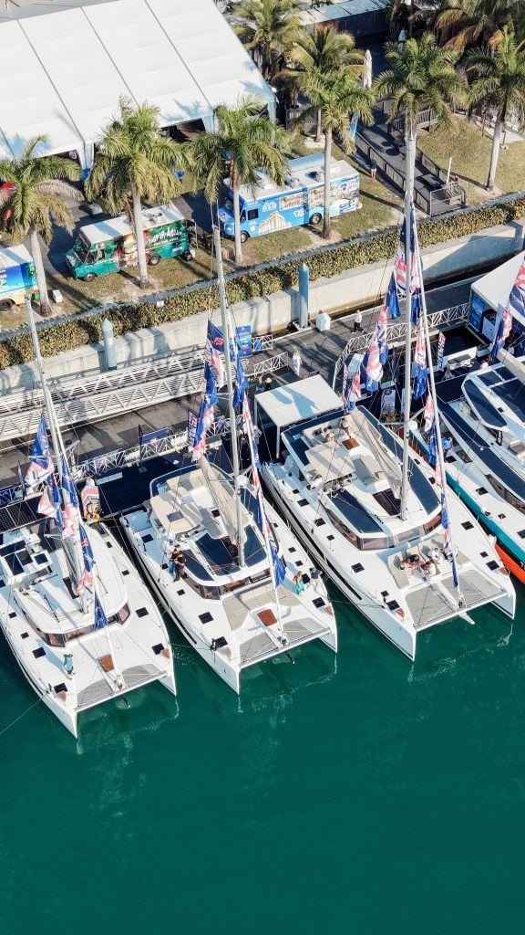 Luxury yachts docked at Miami Boat Show with palm trees and tents in background.