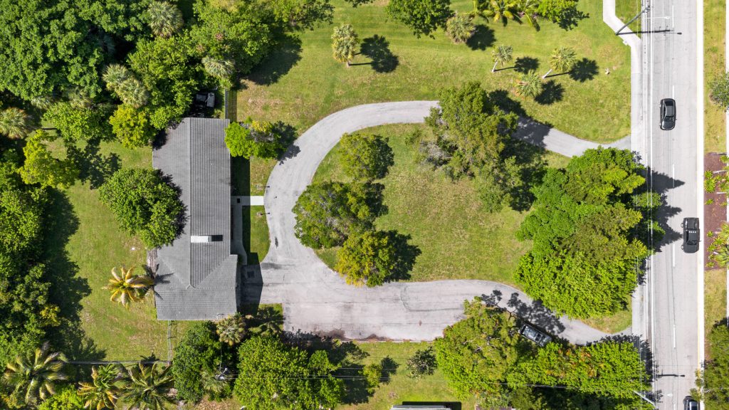 Drone shot of a lush green park with a house and surrounding trees.