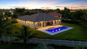 Beautiful suburban house with a lit-up swimming pool and lush green yard during sunset.