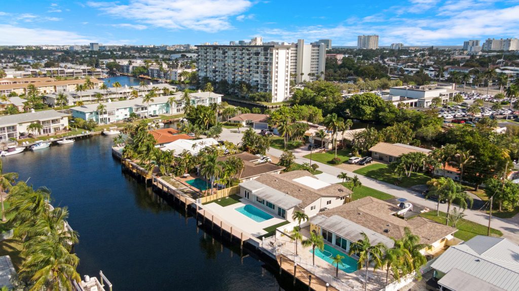 Drone shot of waterfront homes with pool and city skyline in background.