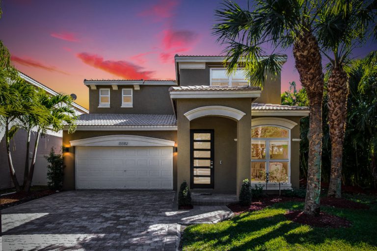 Contemporary house with palm trees and landscaped yard at sunset.