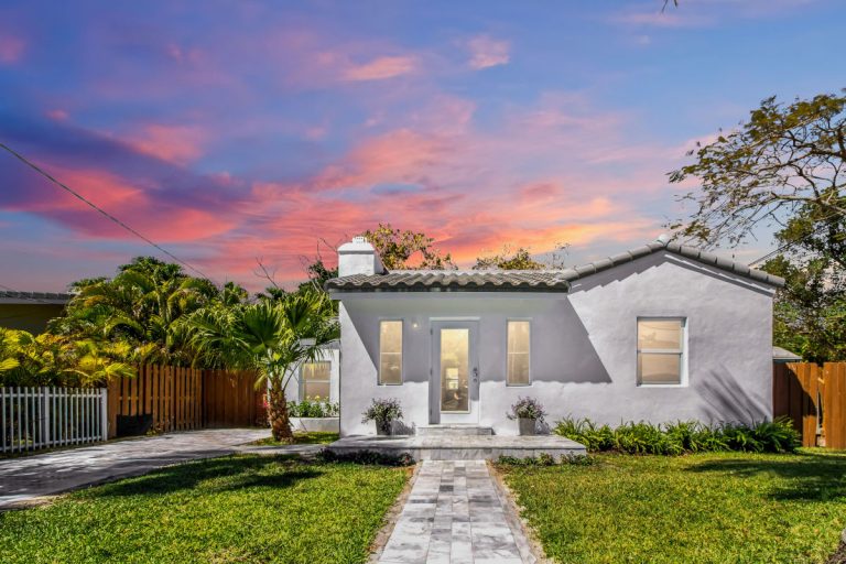 White house with lush landscaping and a vibrant sunset sky in the background.