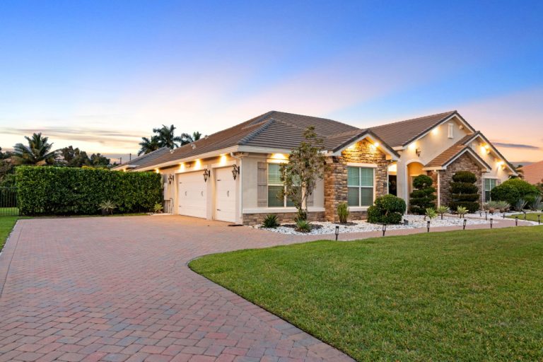 Modern suburban house with landscaped yard, driveway, and exterior lighting at sunset.