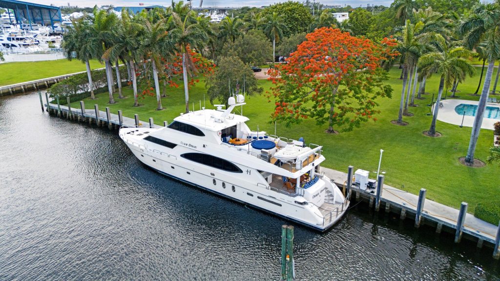 Elegant white yacht moored in a tropical marina with palm trees and colorful foliage.
