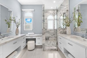 Bright bathroom featuring dual vanities, large mirrors, and a glass-enclosed shower with marble acce.