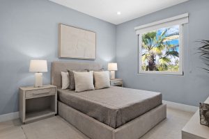 Bedroom with ocean view, tropical palm trees, and bright natural light through window.