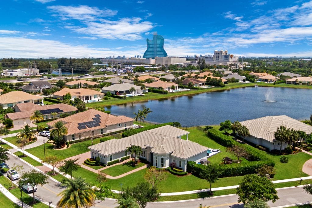 Aerial drone shot of suburban homes and a lake with a city skyline in the background.