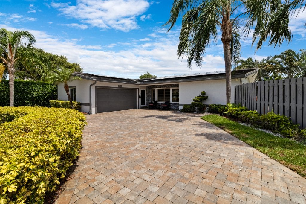 Beautiful single-story home with a paved driveway and tropical landscaping.