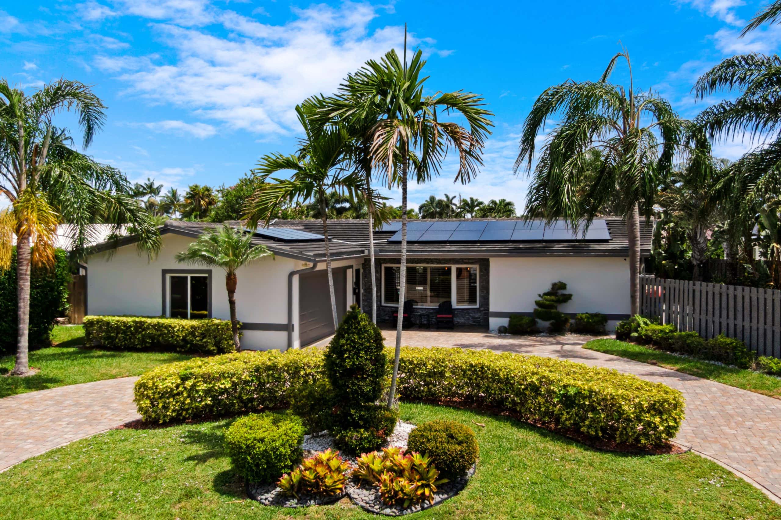 Tropical home with lush landscaping and palm trees in front yard.