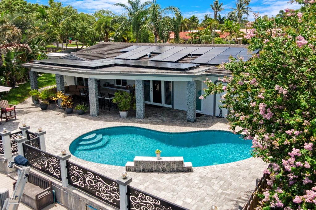 Luxury home with solar panels, pool, and lush landscaping in a tropical setting.