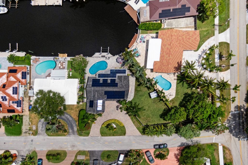 Aerial view of a waterfront property with multiple pools and lush landscaping.