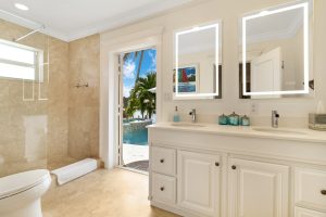 Bathroom with double vanity, large mirrors, and outdoor view through open door.