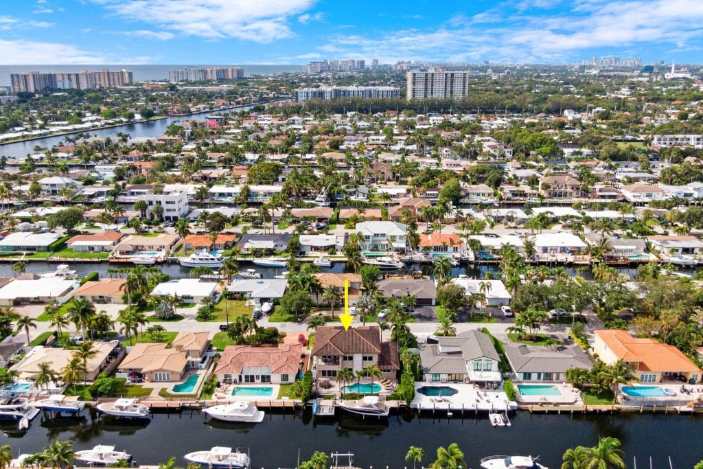 Drone shot of waterfront homes and boats in a sunny residential area.