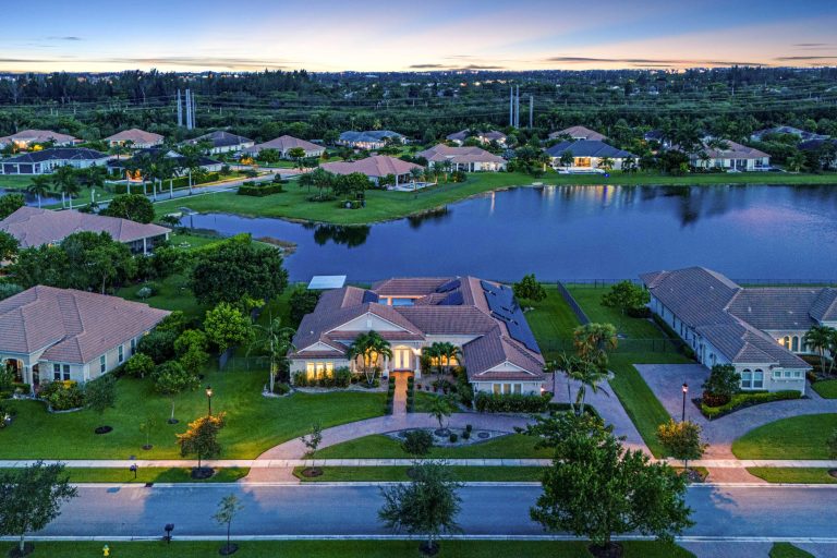 Aerial view of a luxury lakeside residential community with modern homes and lush greenery at sunset.