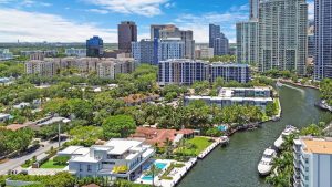 Aerial view of Miami skyline featuring high-rise buildings, waterfront homes, and a river with boats.