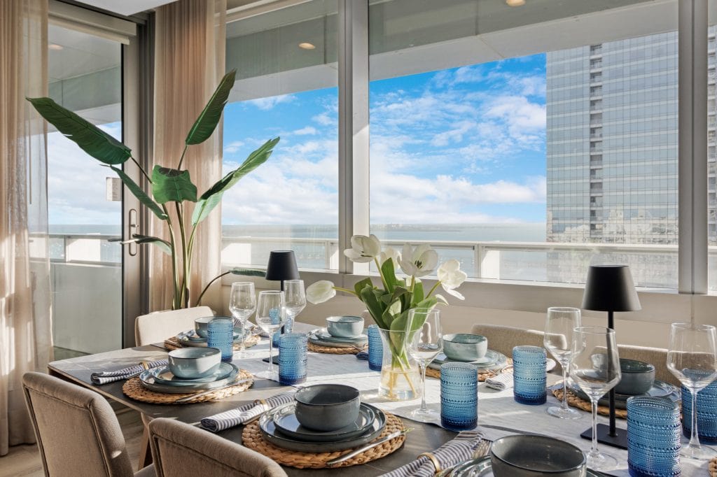 Elegant dining table set with blue glassware and white flowers, overlooking city skyline.