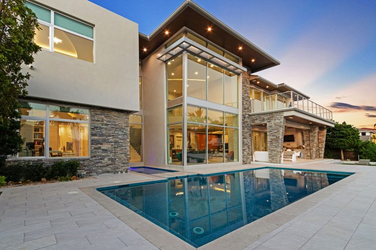 Contemporary house with pool, glass walls, and modern architecture at sunset.