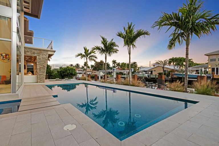 Outdoor swimming pool surrounded by palm trees and modern homes.