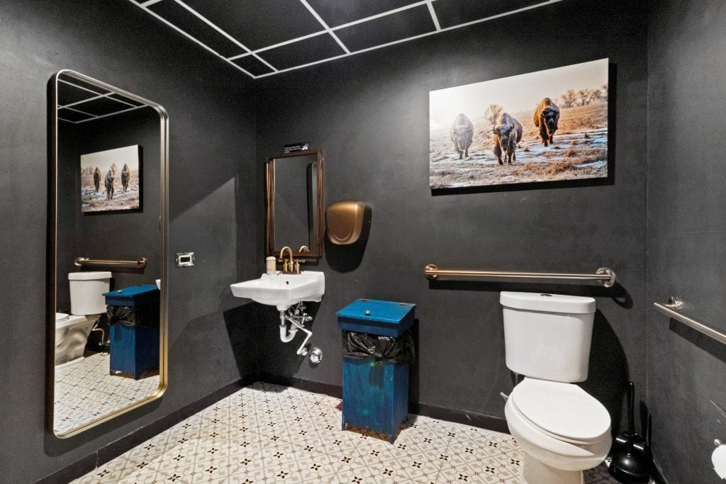 Accessible restroom with grab bars, sink, mirror, and artwork on dark walls for comfort and safety.