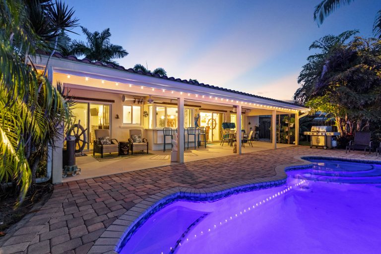 Outdoor pool with LED lighting and patio furniture in a tropical backyard setting.