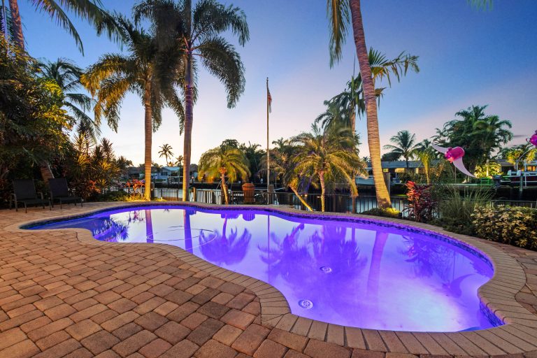 Pool with illuminated water and tropical palm trees at sunset.