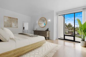 Spacious bedroom featuring a large glass door opening to a tropical outdoor scene with palm trees an.
