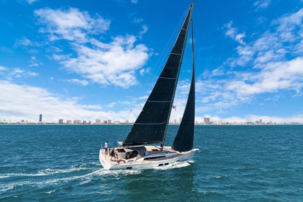 Sailing yacht with black sails on blue ocean under clear sky, city skyline in background.