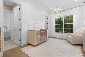 Nursery room with large window, white walls, and cozy furniture for a comfortable baby space.