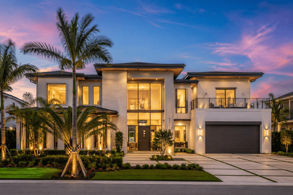 Elegant contemporary mansion featuring large glass windows and lush landscaping at dusk.