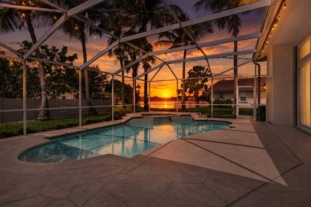 Beautiful sunset over enclosed backyard pool with palm trees.
