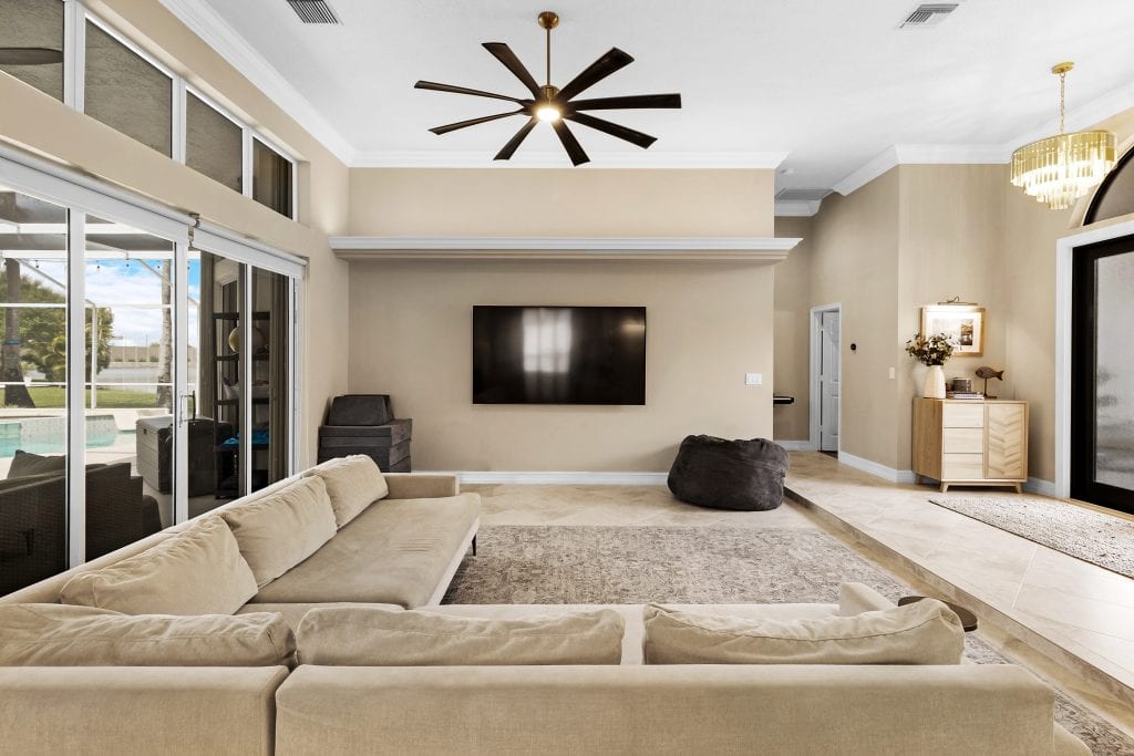Spacious modern living room with beige sofa, wall-mounted TV, and large windows.