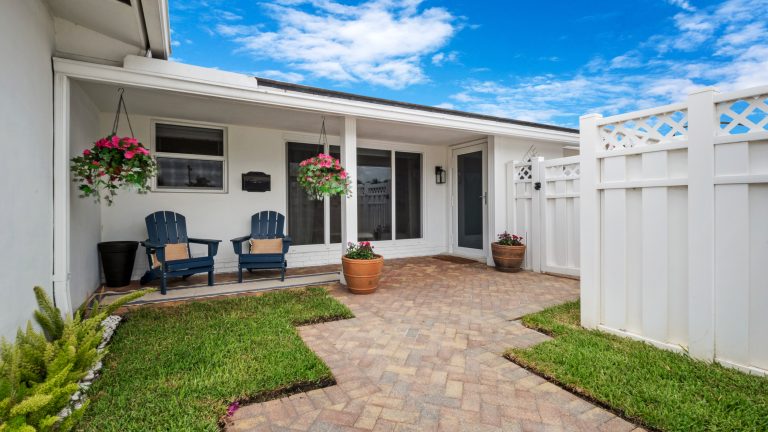 Outdoor patio with two chairs, potted plants, and a white fence under a blue sky.