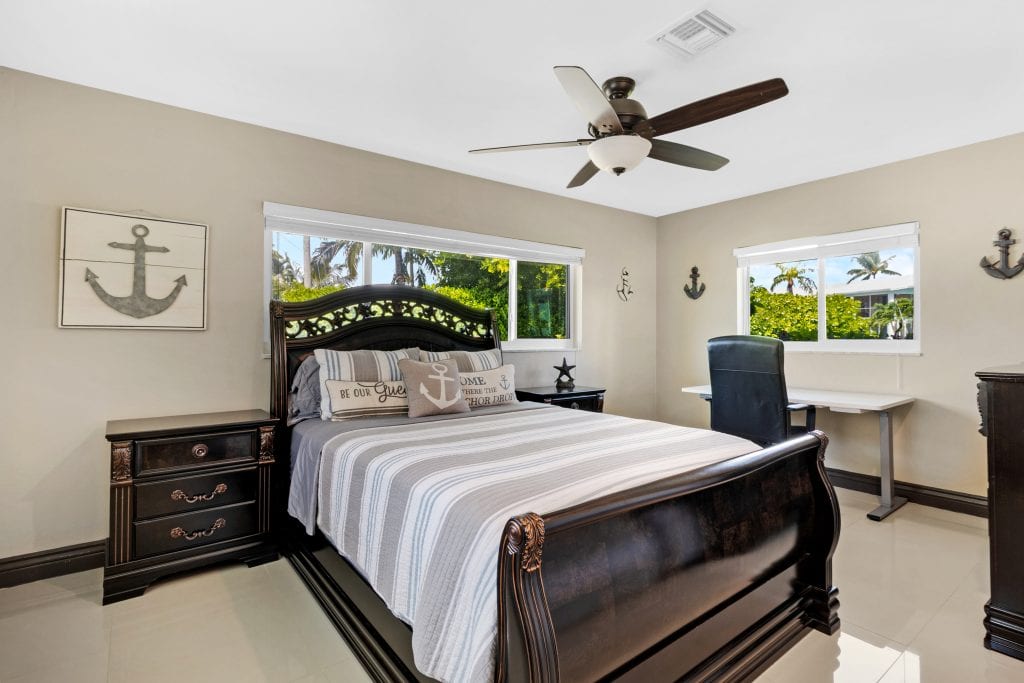 Spacious bedroom with nautical decor, large windows, and modern ceiling fan.