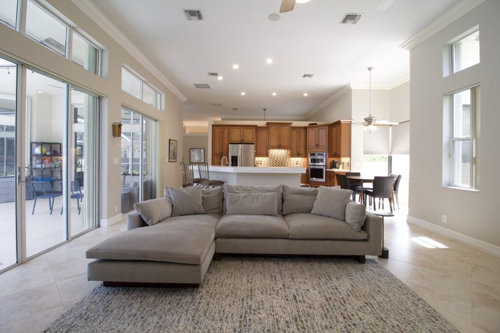 Bright living room with large windows, beige sofa, and open kitchen area.