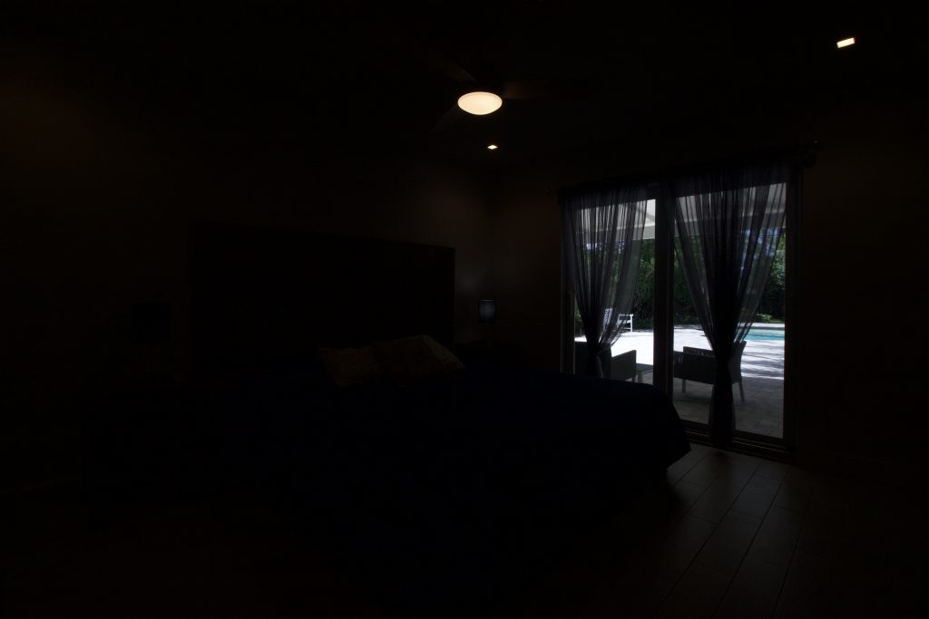 Dark bedroom with large window showing outdoor view, low lighting.