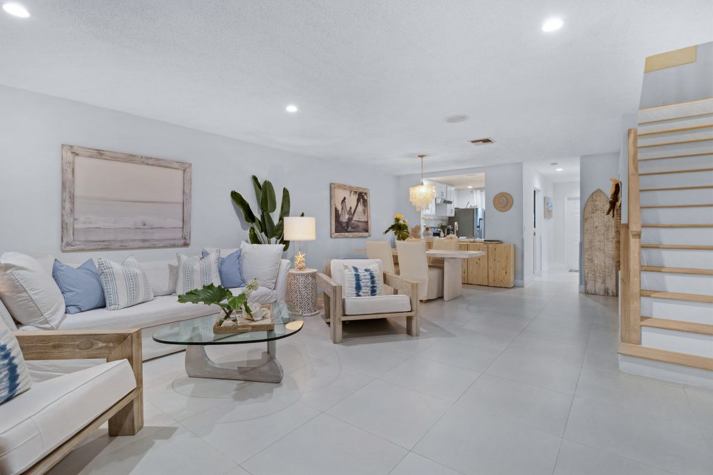 Spacious coastal living room with white walls, wooden furniture, and ocean-themed decor.