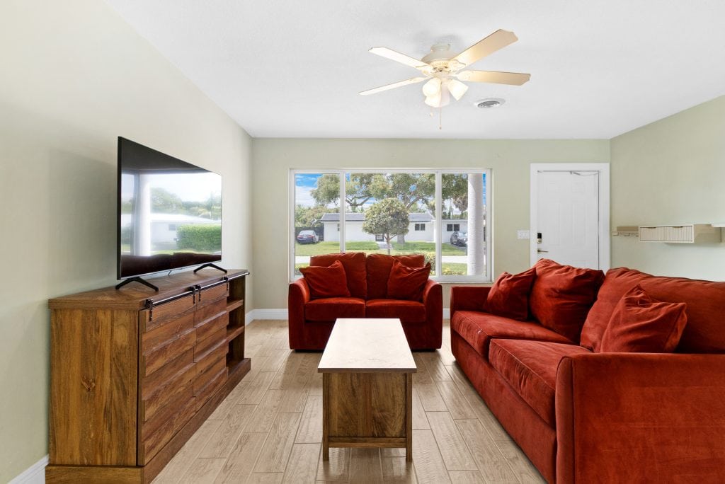 Bright living room with red sofas, TV, and large window overlooking yard.