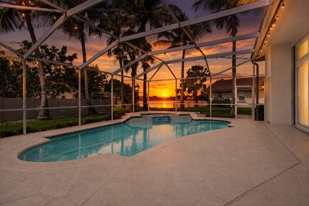 Beautiful sunset over screened pool enclosure with tropical trees.