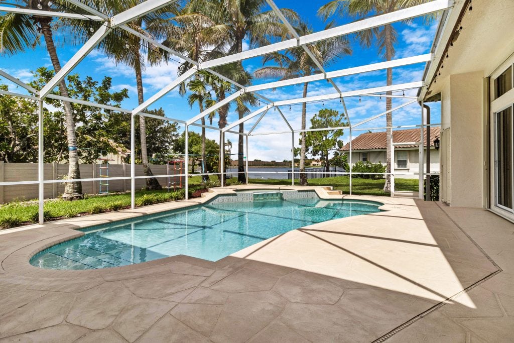 Pool area with screened enclosure, palm trees, and blue sky.