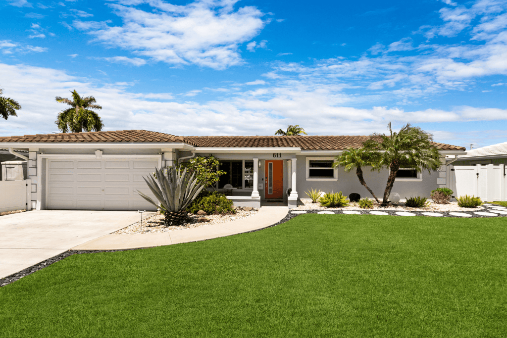 Beautiful single-story house with lush front yard and palm trees under a blue sky.