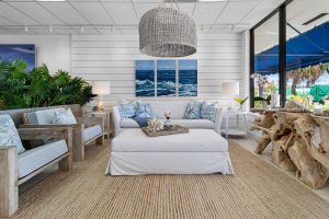 Bright coastal living room with white furniture, blue accents, and ocean view artwork.