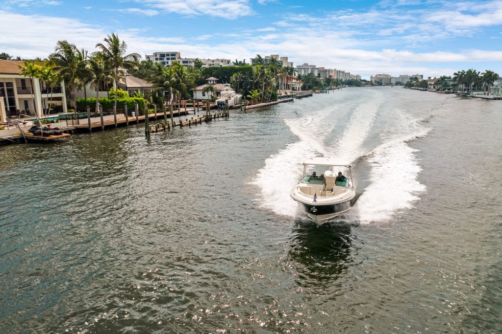 Speedboat cruising on a scenic waterway with waterfront homes and palm trees.