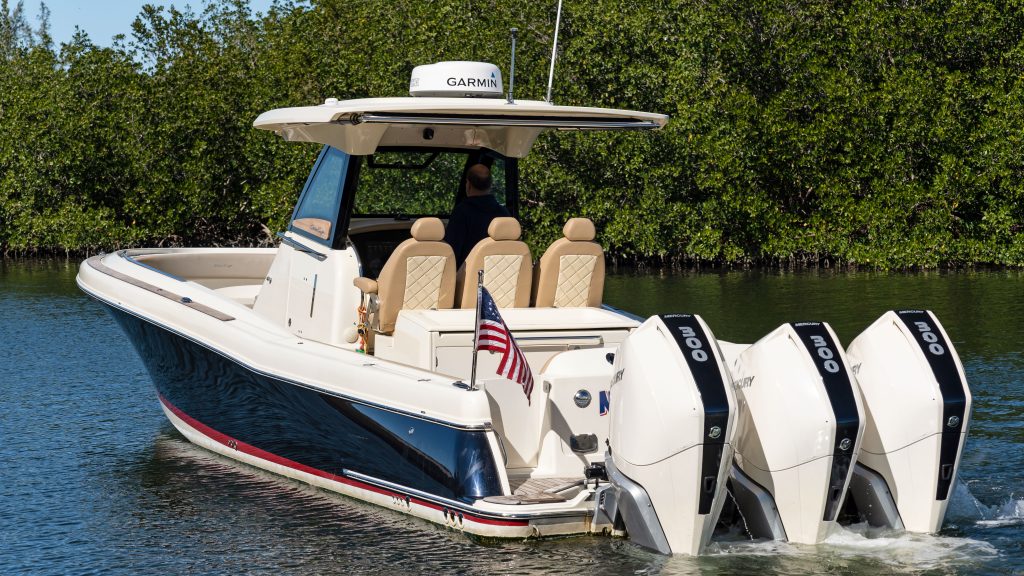 Powerboat with twin engines cruising on water near lush greenery.